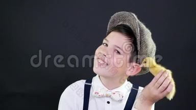肖像，一个戴着帽子和吊带的漂亮男孩和一只黄色的小鸭子玩.. 专题装饰的工作室视频